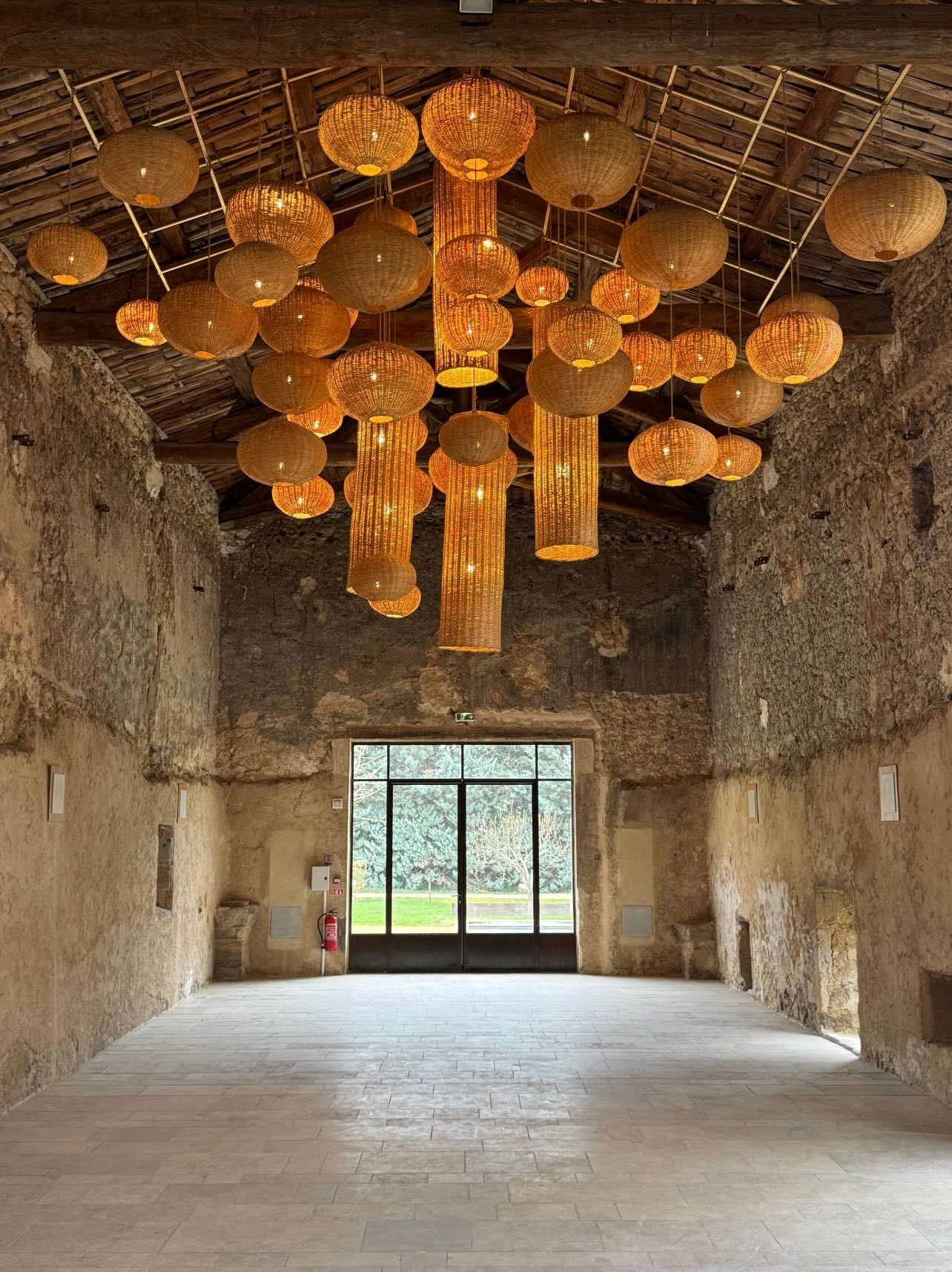 Rustic stone hall with woven rattan pendant lights hanging from wooden ceiling, large glass doors opening to garden.