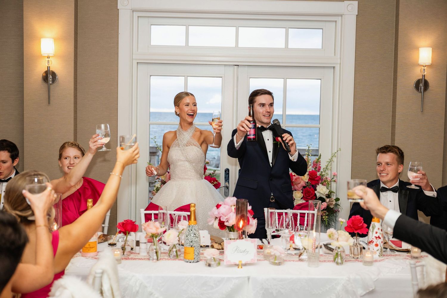 Bride in layered white gown and groom in black tuxedo toast in an elegant Lake Michigan wedding at The Inn at Bay Harbor.
