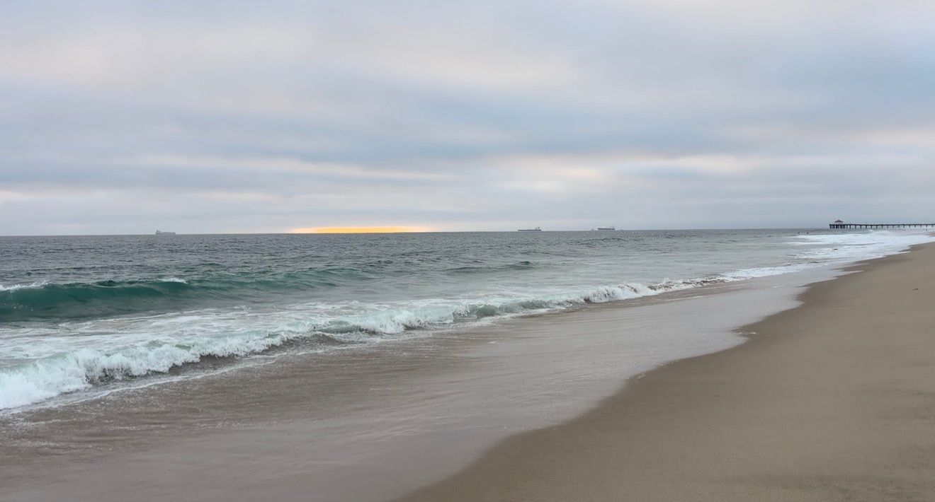 Calm ocean waves gently washing onto a sandy beach under a cloudy sky with a faint sunset glow on the horizon.