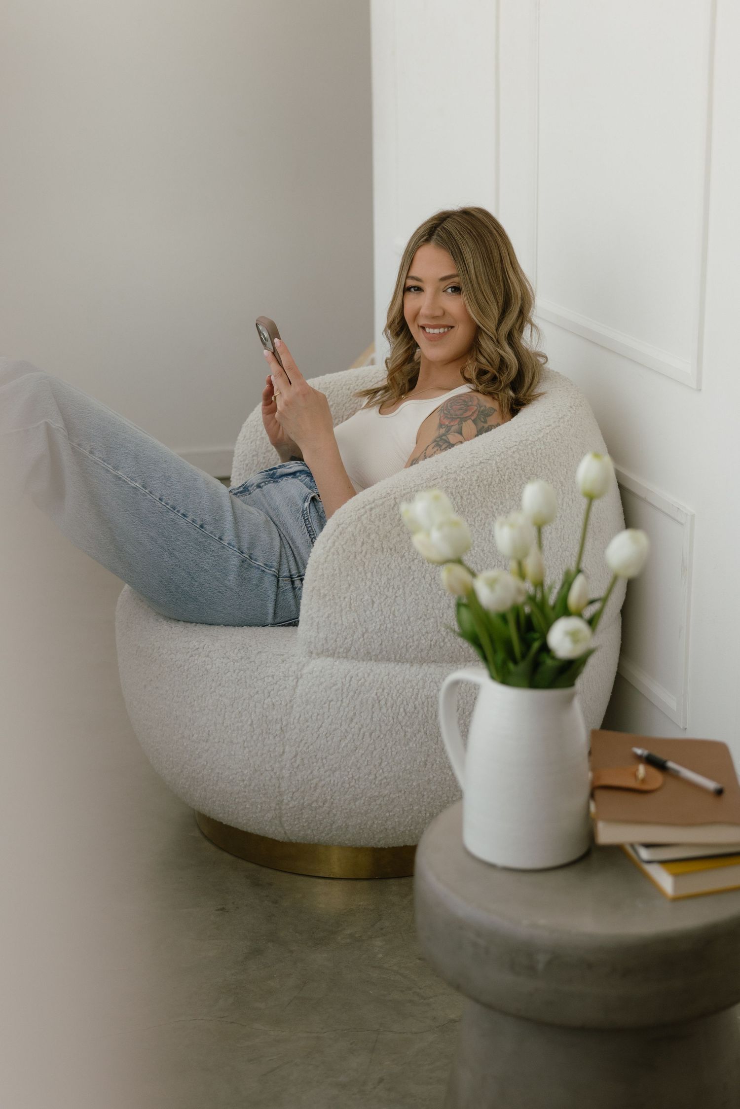 Smiling woman in white blazer and jeans using smartphone against dark background.