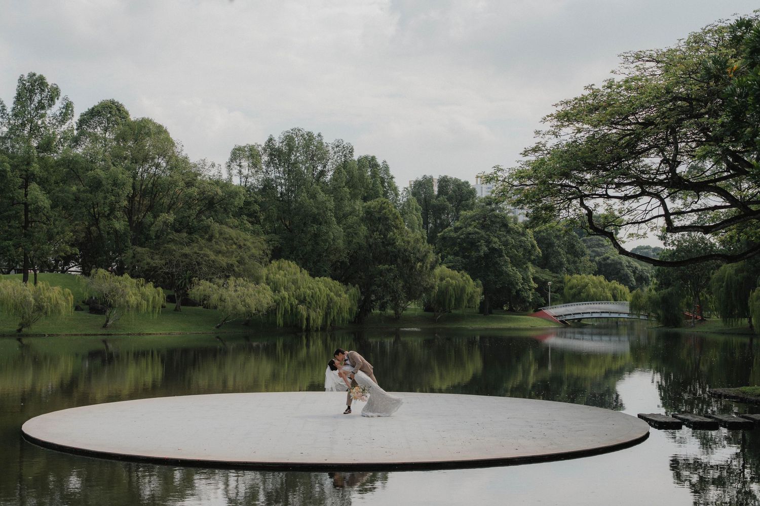 Scenic panoramic view of a tranquil lake surrounded by lush green trees and vegetation on a cloudy day.