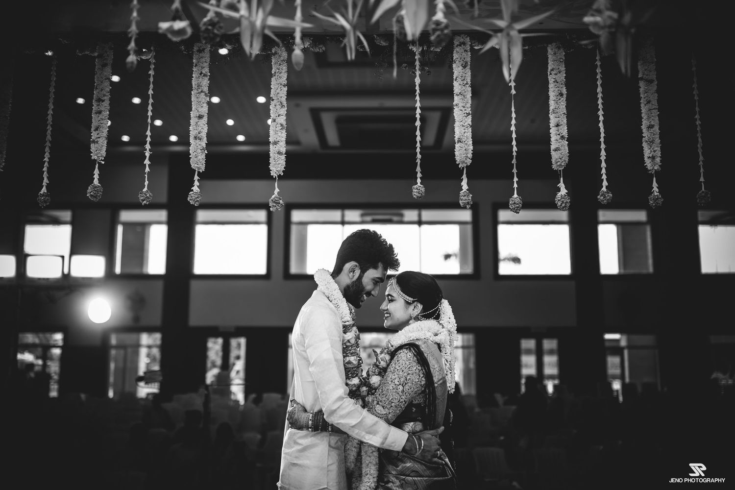 Romantic black and white photo of a couple embracing under hanging decorative lights.