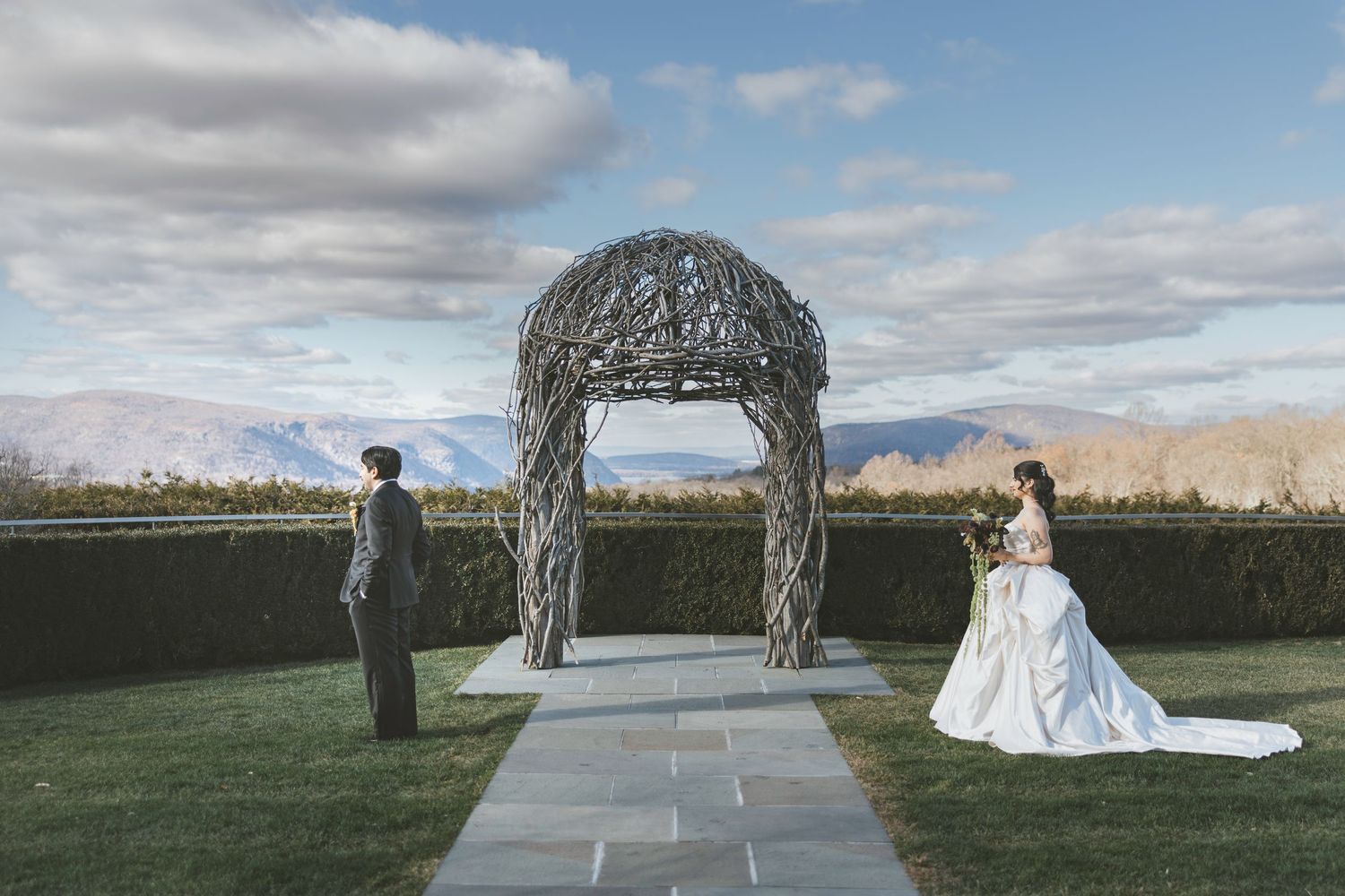Outdoor wedding ceremony takes place on lawn in front of grand stone castle with Gothic architecture under cloudy skies.