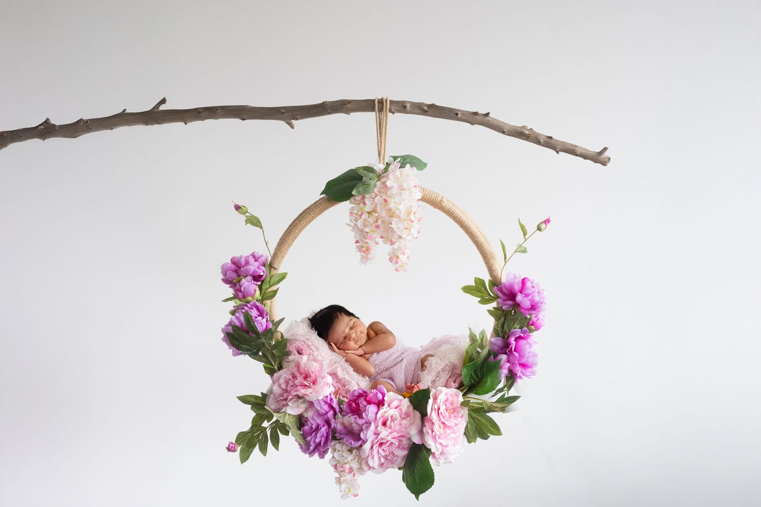 A delicate floral hoop wreath made with pink peonies and greenery hangs against a white wall.