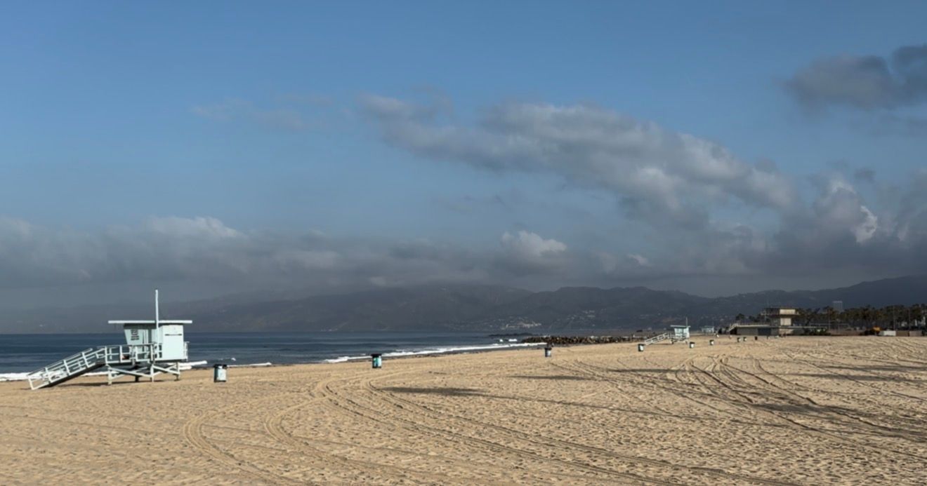 A light blue lifeguard tower stands on a sandy beach with calm ocean waters and a partly cloudy sky in the background.