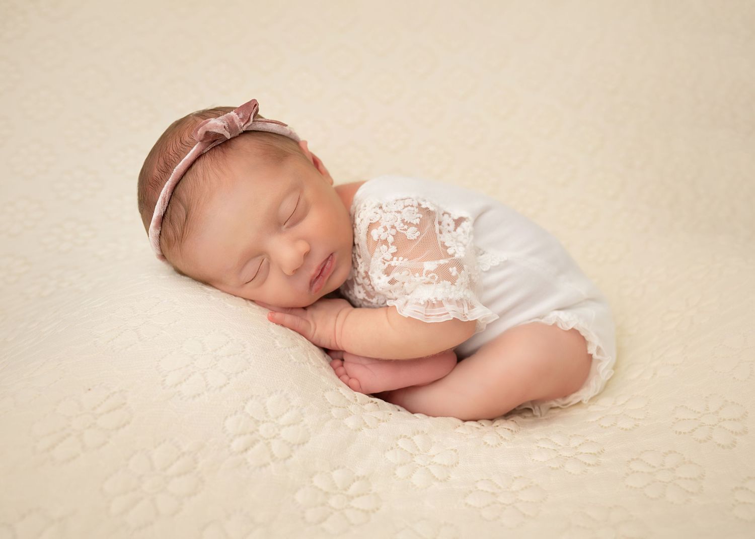 Newborn baby girl posed on a cream backdrop during a newborn photography session