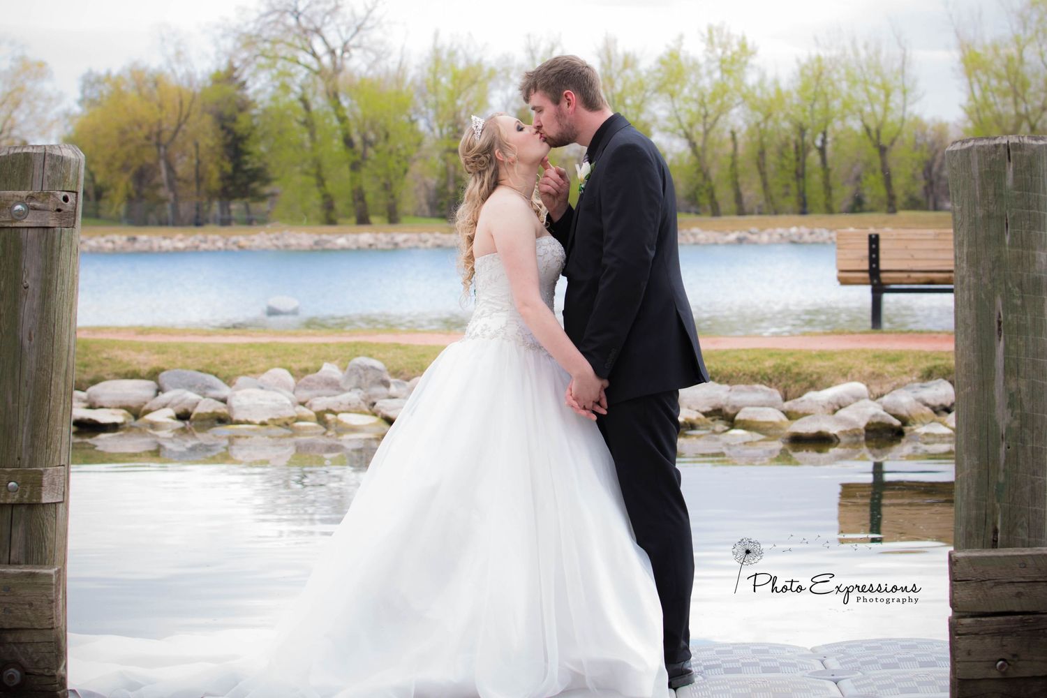 Wedding couple poses on wooden dock by water during overcast day.