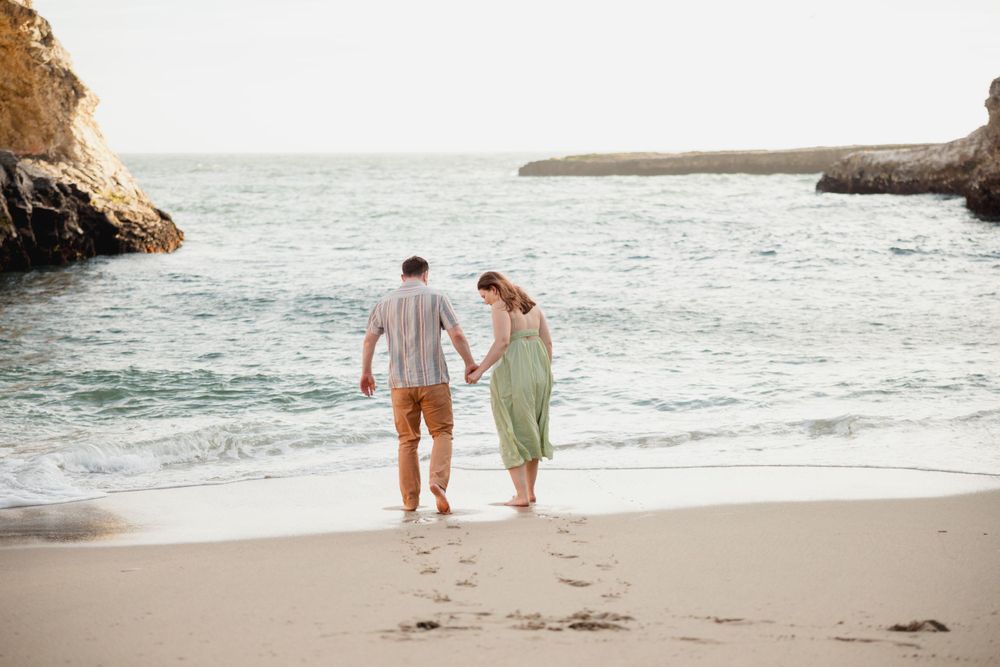 A couple walks hand in hand along a secluded beach cove at sunset.