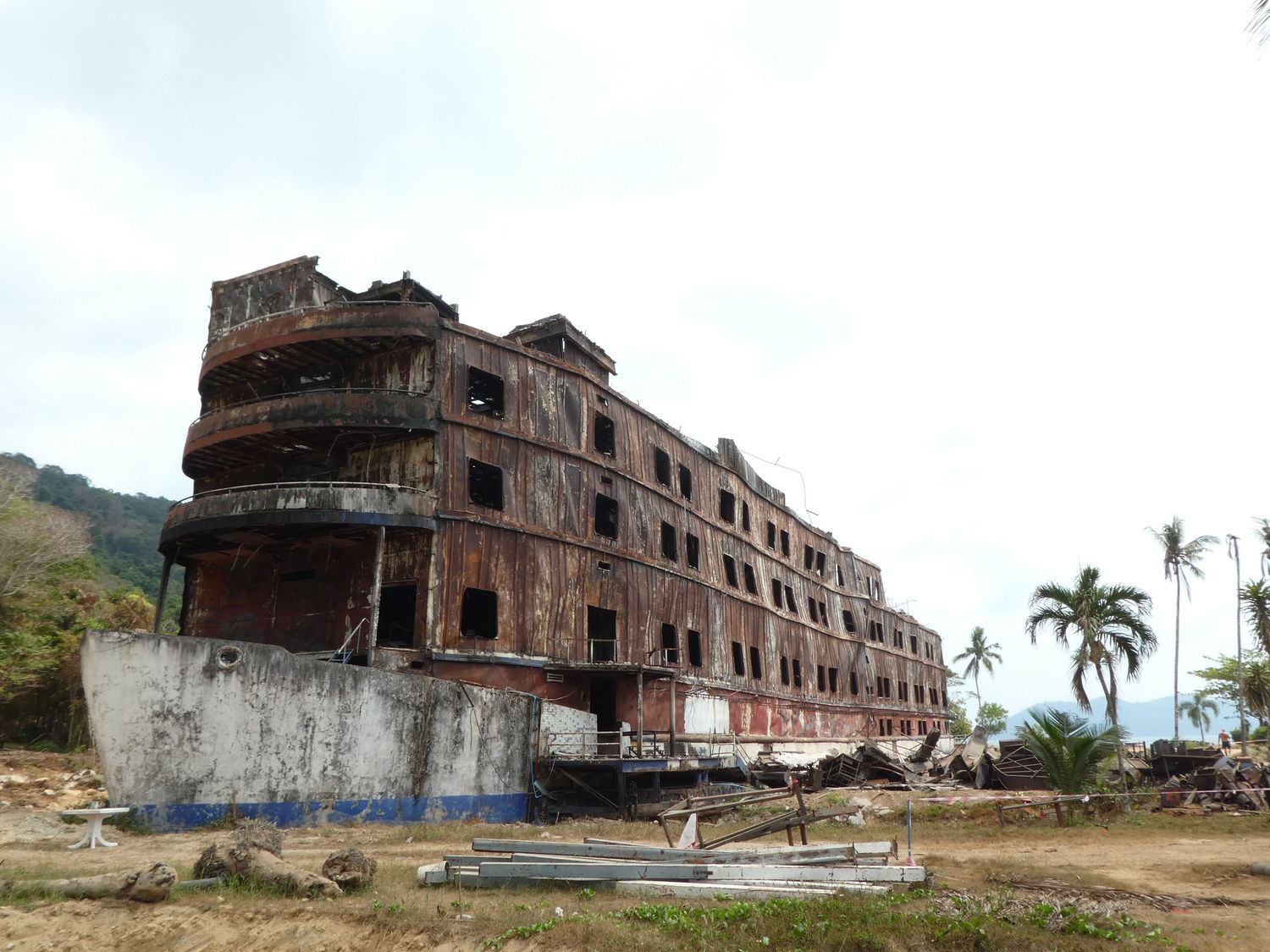 Abandoned and damaged multi-story brick hotel building with palm trees visible in tropical coastal setting.