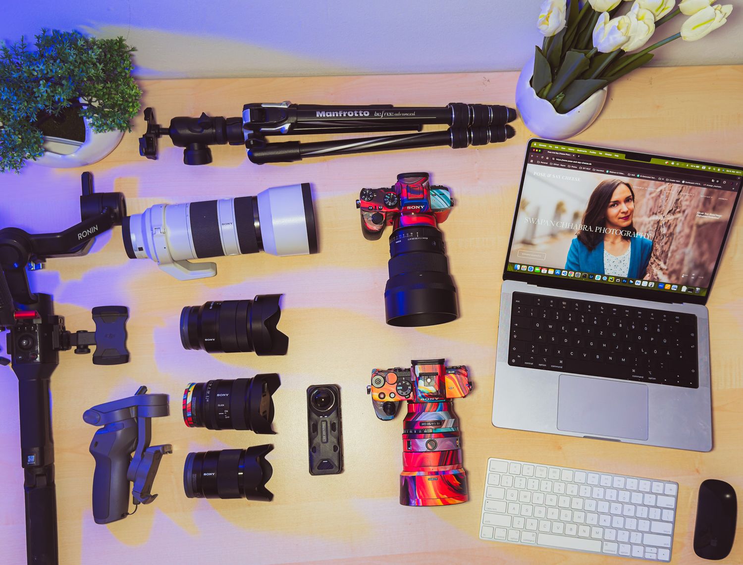 Professional photography equipment including cameras, lenses, tripod and laptop laid out on white surface.