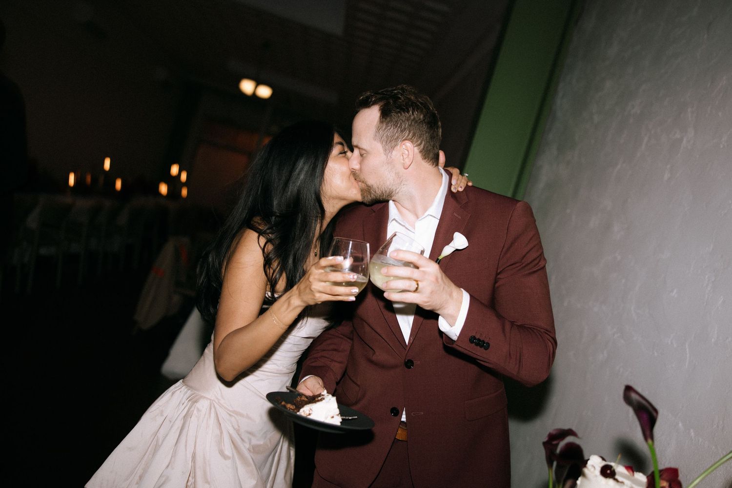 Bride and groom share a champagne kiss at their wedding reception in warm ambient lighting.