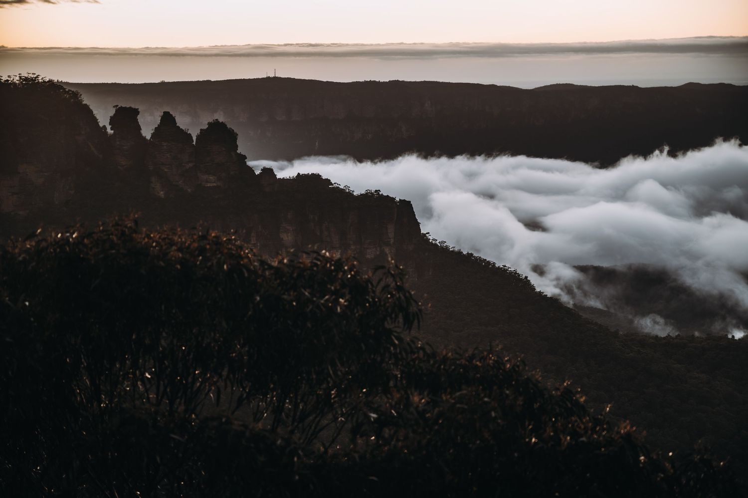Dramatic mountain landscape with low-lying clouds rolling through valleys at sunset.