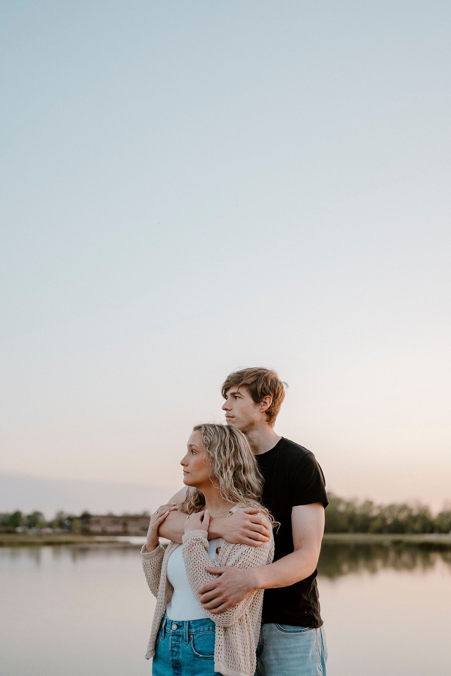 A romantic couple embraces by a serene lake at sunset, creating an intimate silhouette against the calm water.