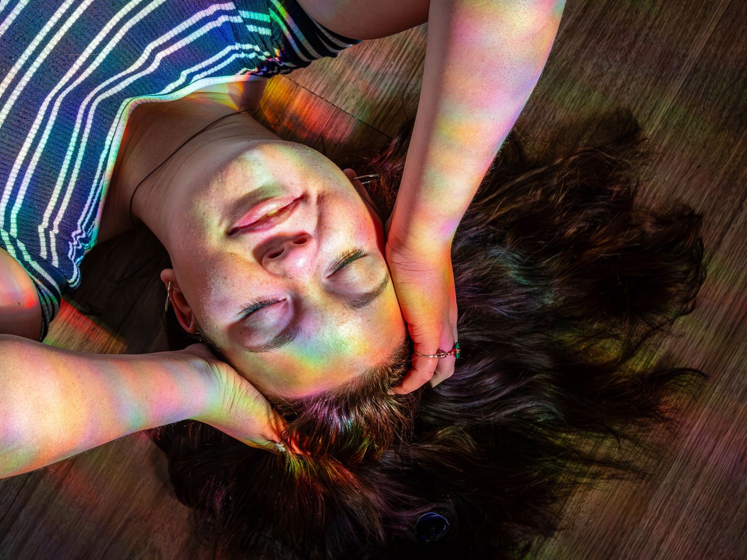 High angle view of someone lying on wooden floor with hands on face in colorful lighting.