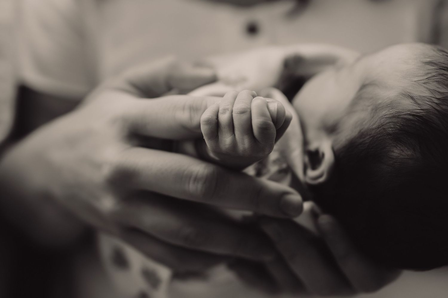 black and white image -a close up of a newborn baby gripping the pinky finger of an adult