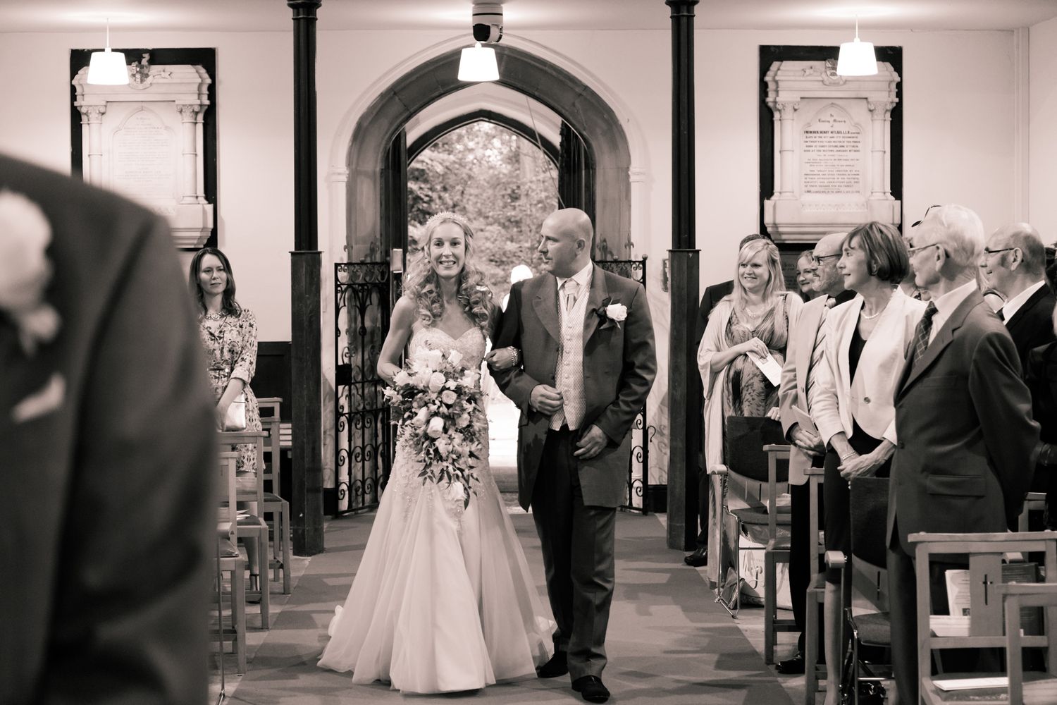 A black and white photo of a wedding ceremony inside a traditional church with arched doorways.