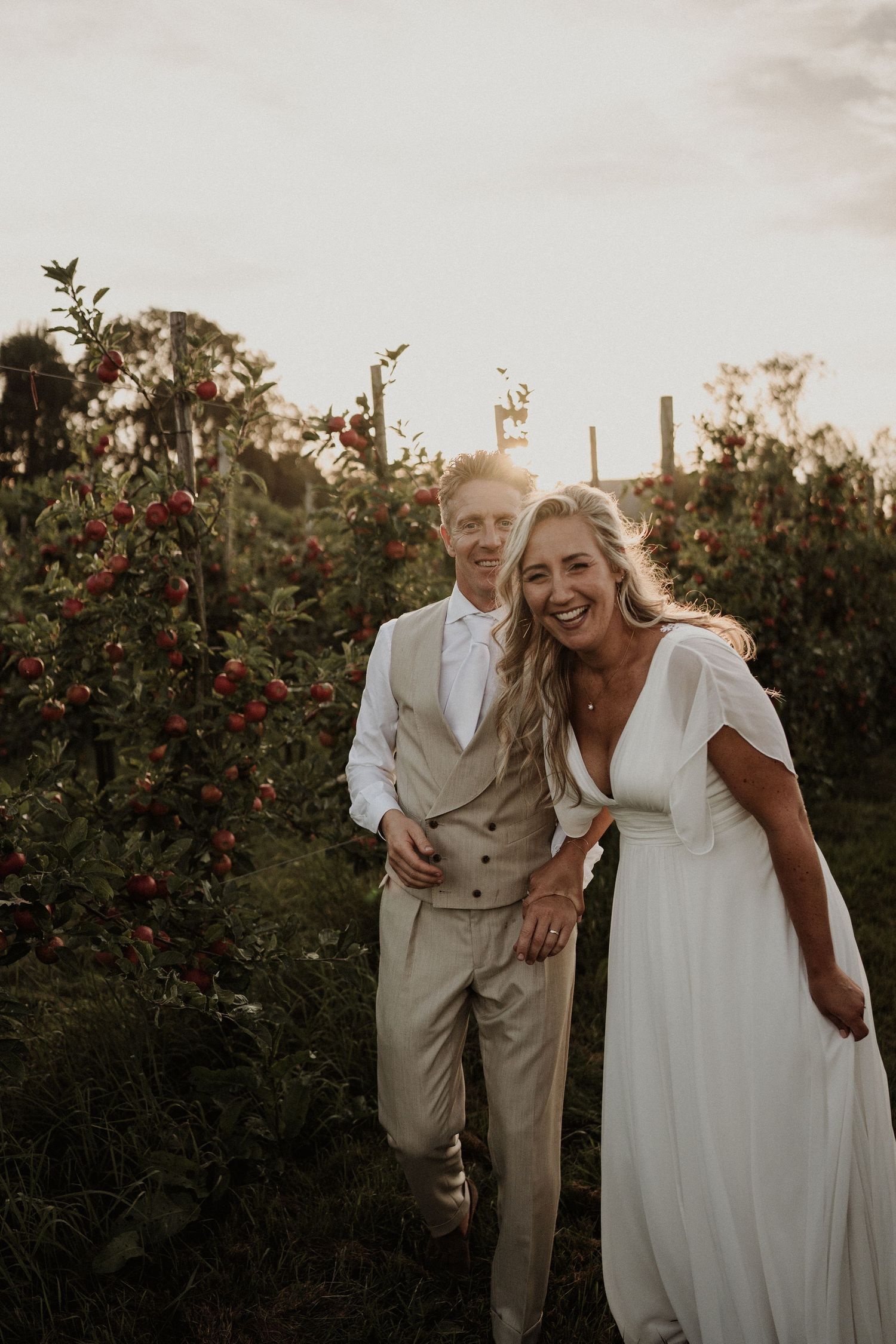 A couple shares a joyful moment together in a garden with red flowers at sunset.