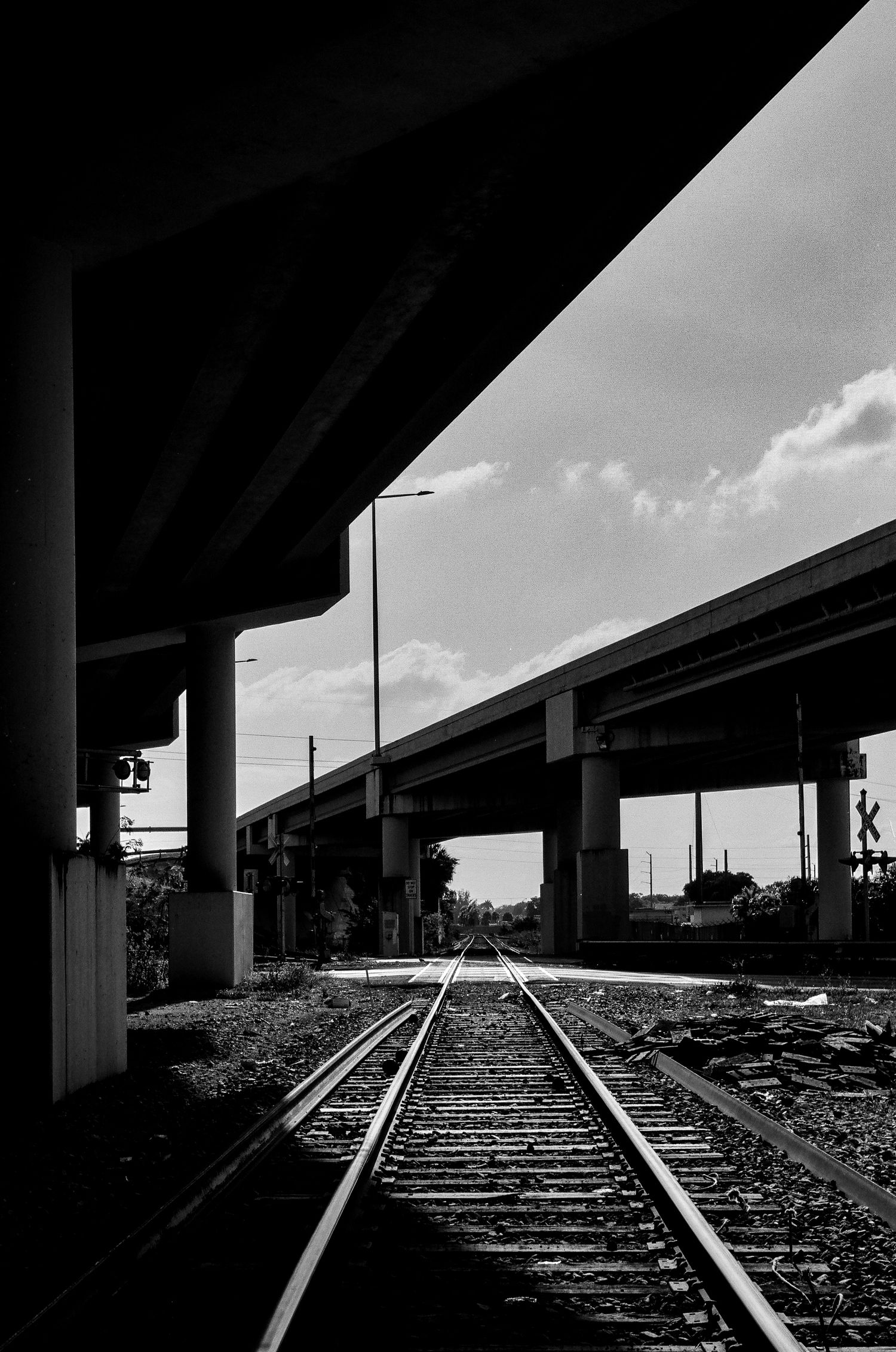 Black and white photo of train tracks leading under highway overpasses.
