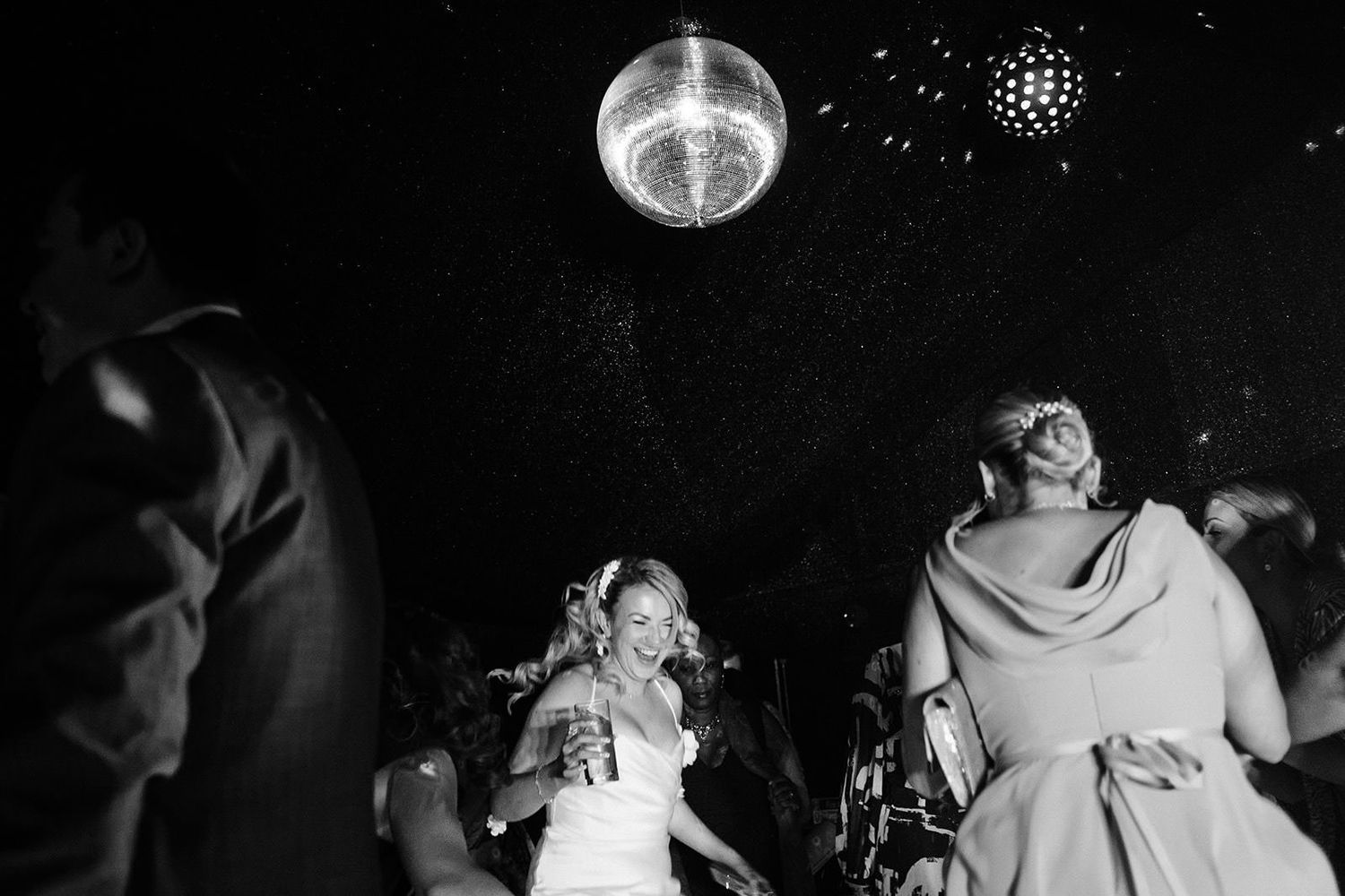 Wedding reception dance party under disco ball lights in dark venue.