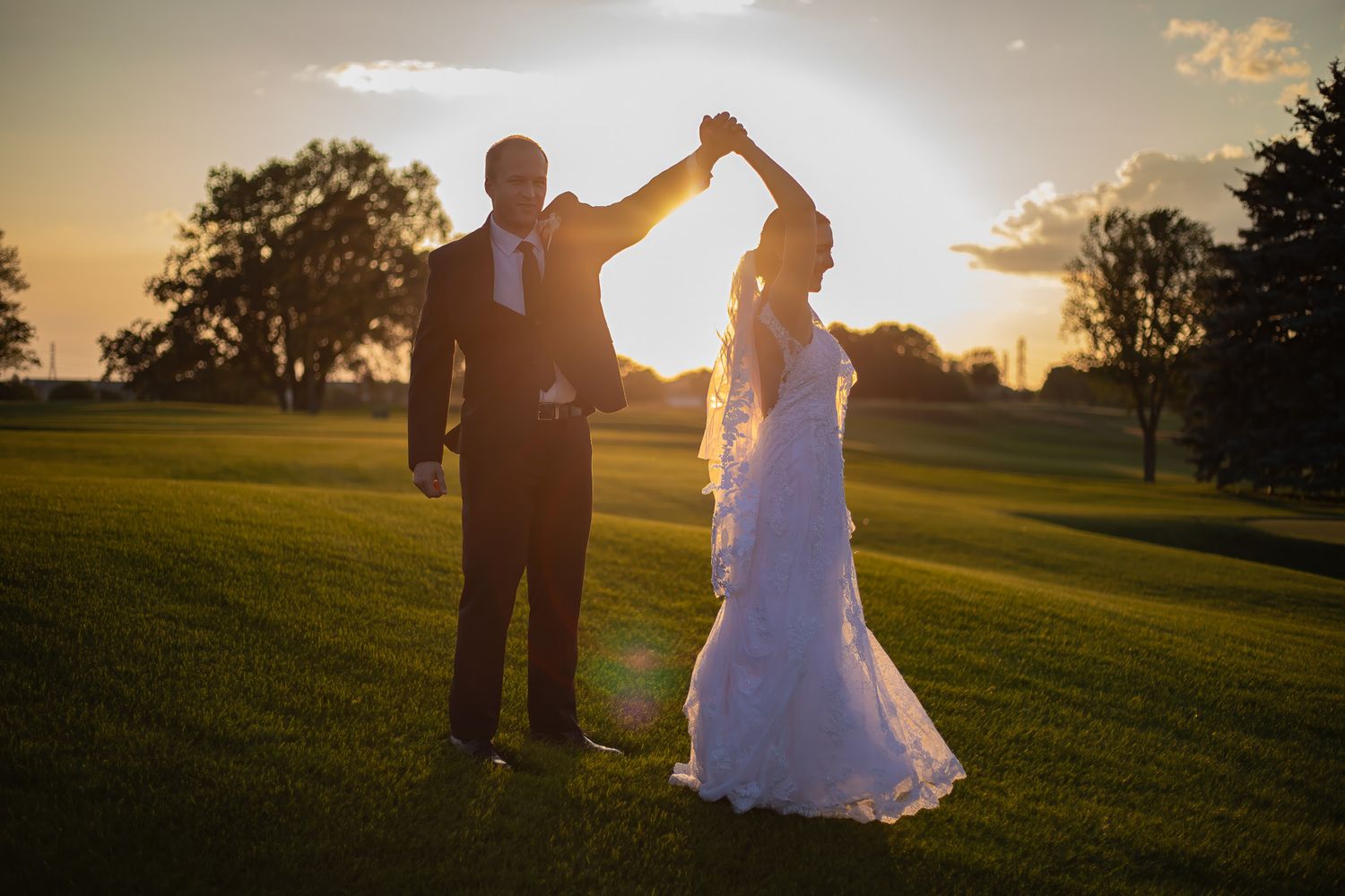 Couple dancing at sunset in an open field with golden light.