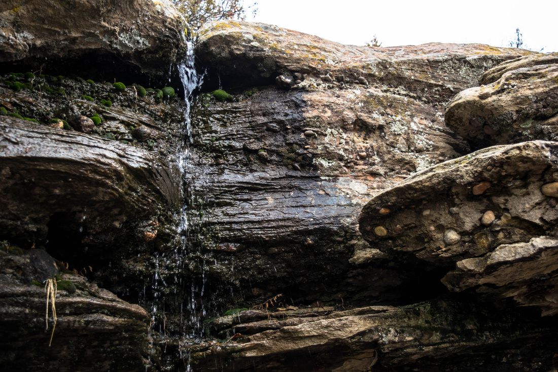 A scenic waterfall cascades down layered rock formations in a natural cave setting.