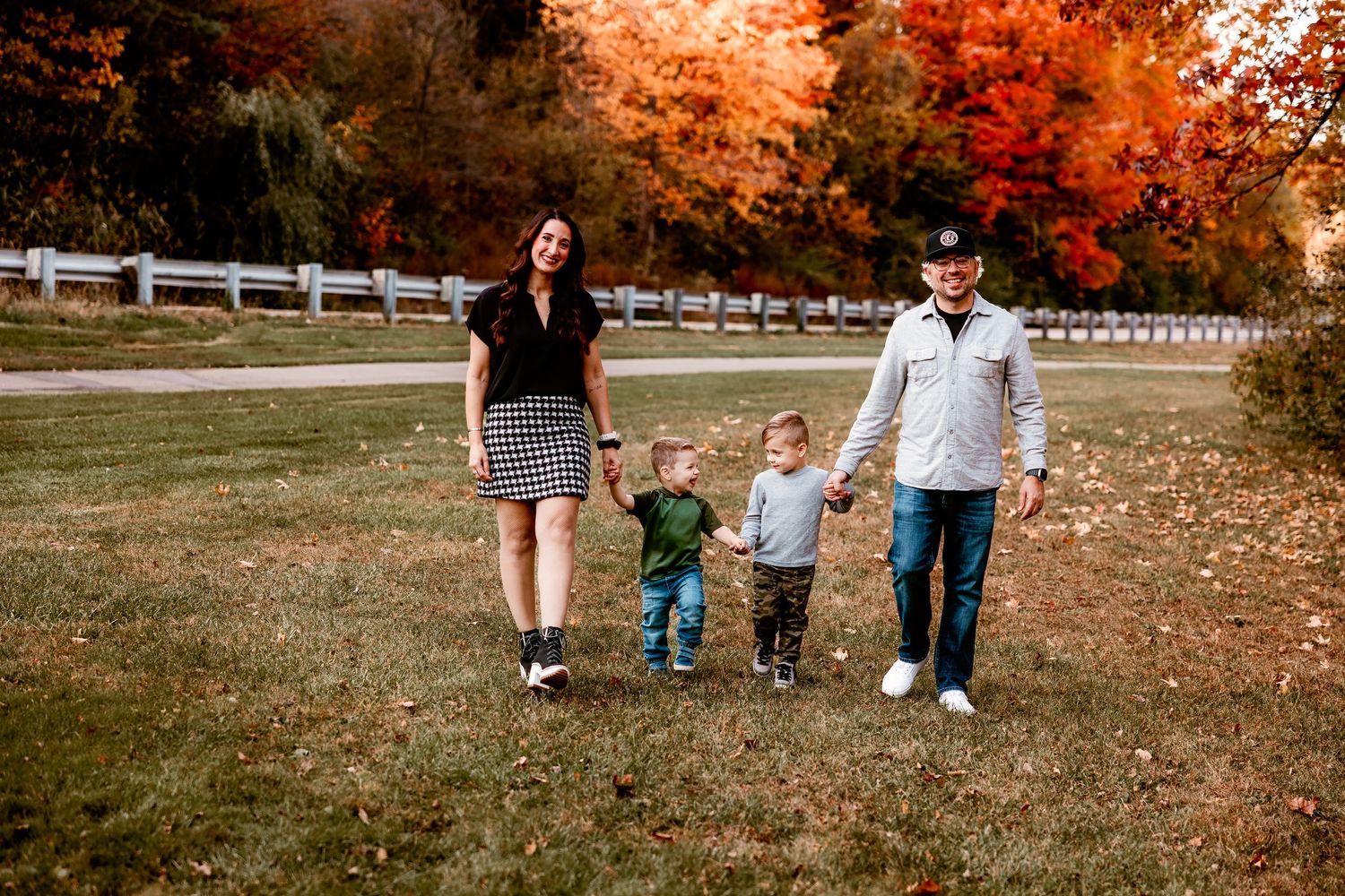 A family walks hand in hand along a path surrounded by vibrant fall foliage and a winding fence in Northville Michigan
