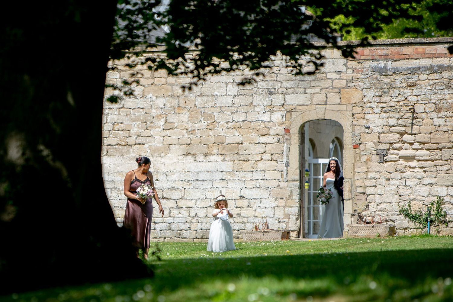 Wedding scene at a stone castle wall with figures visible through an archway door by Nova Scotia wedding photographer