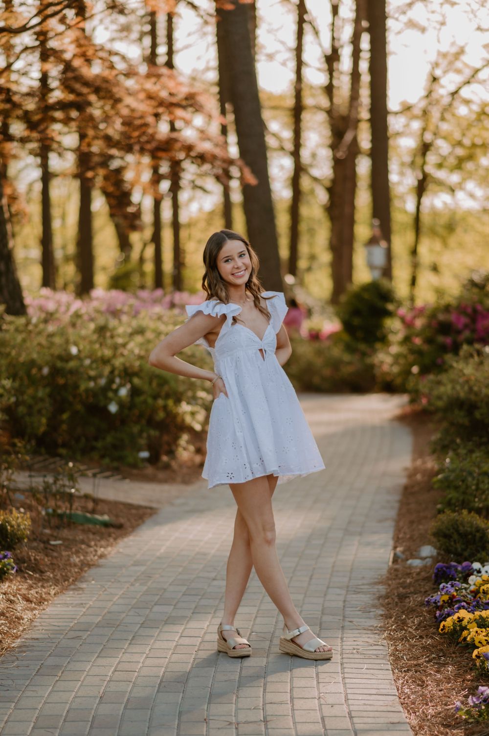 White sundress twirling pose on garden path surrounded by spring flowers.