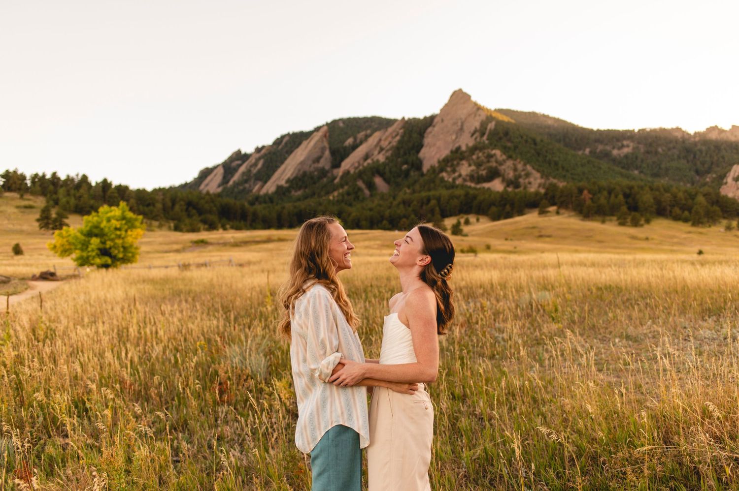 Two people sharing a sweet moment in a field with the Flatirons mountains in the background.
