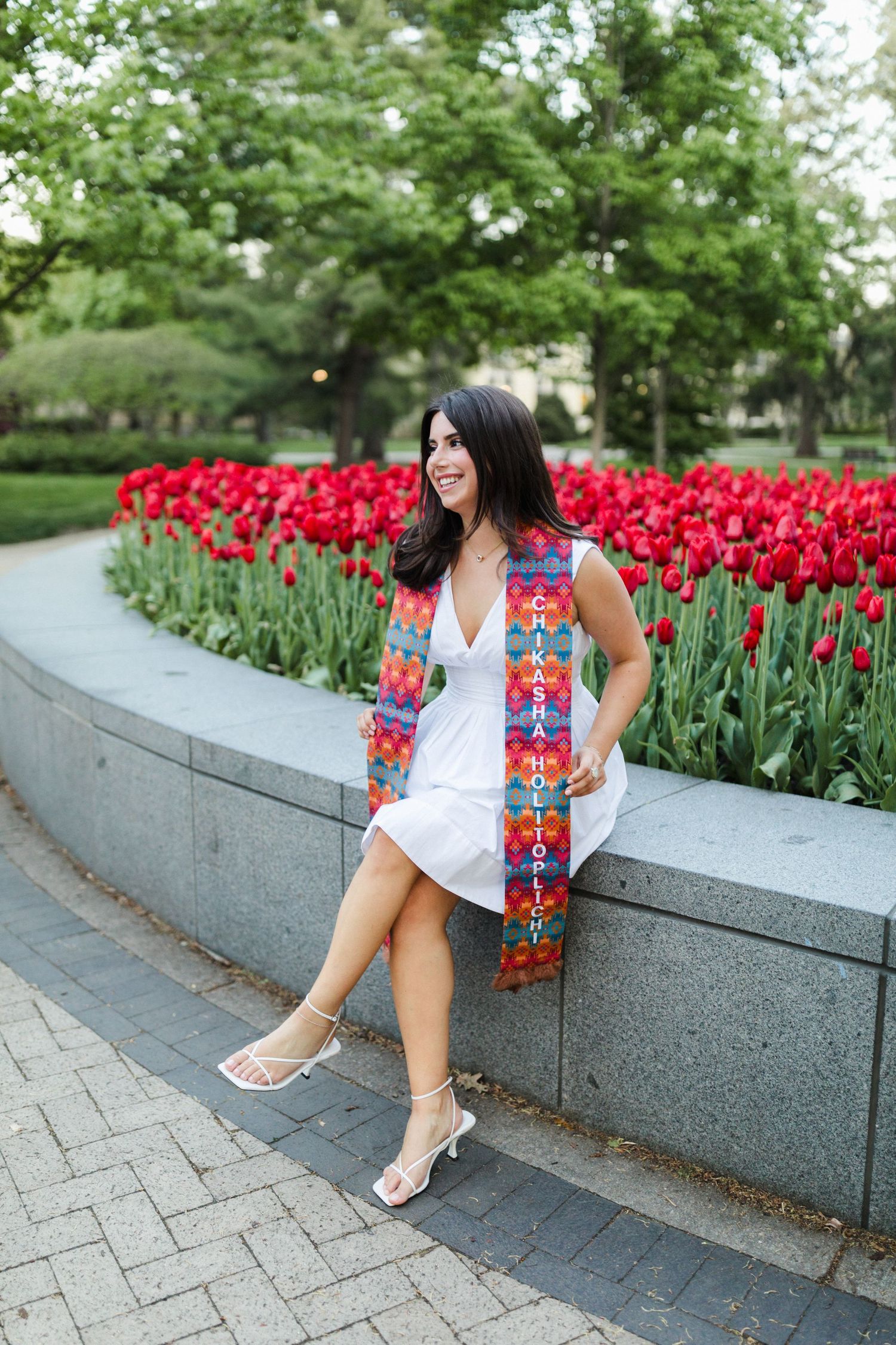A white summer dress and colorful scarf against vibrant red tulips in a garden setting.