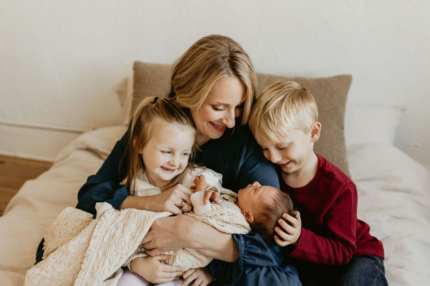 A family gathers together on a cozy couch sharing a tender moment with a newborn baby wrapped in blankets.  Tulsa newborn photographer.