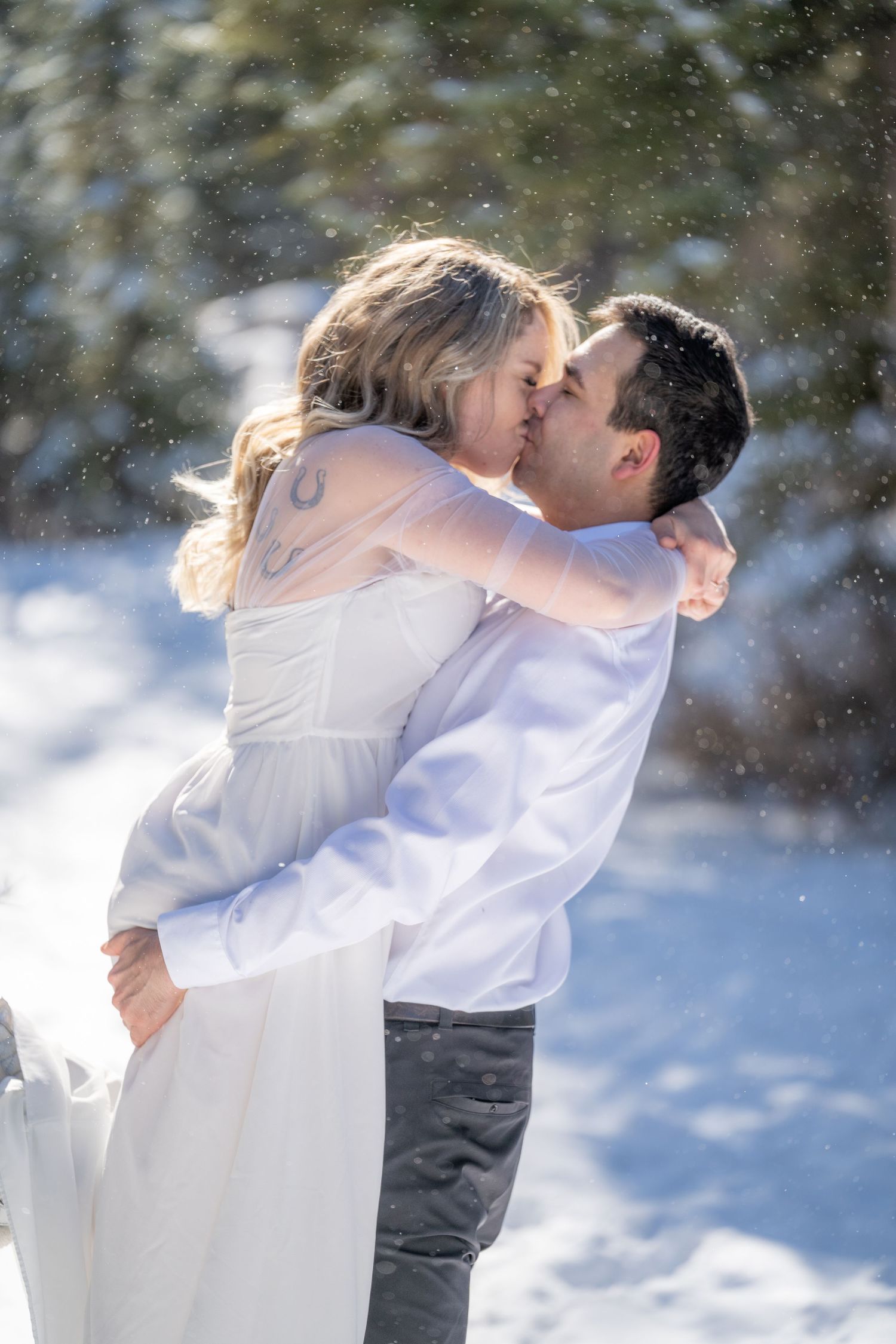 A romantic winter wedding scene with a couple embracing and kissing in falling snow.