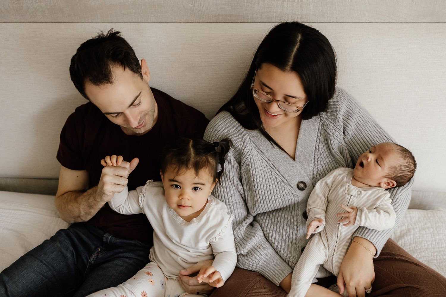 A family with a toddler and newborn snuggle together on their bed for a lifestyle newborn photoshoot