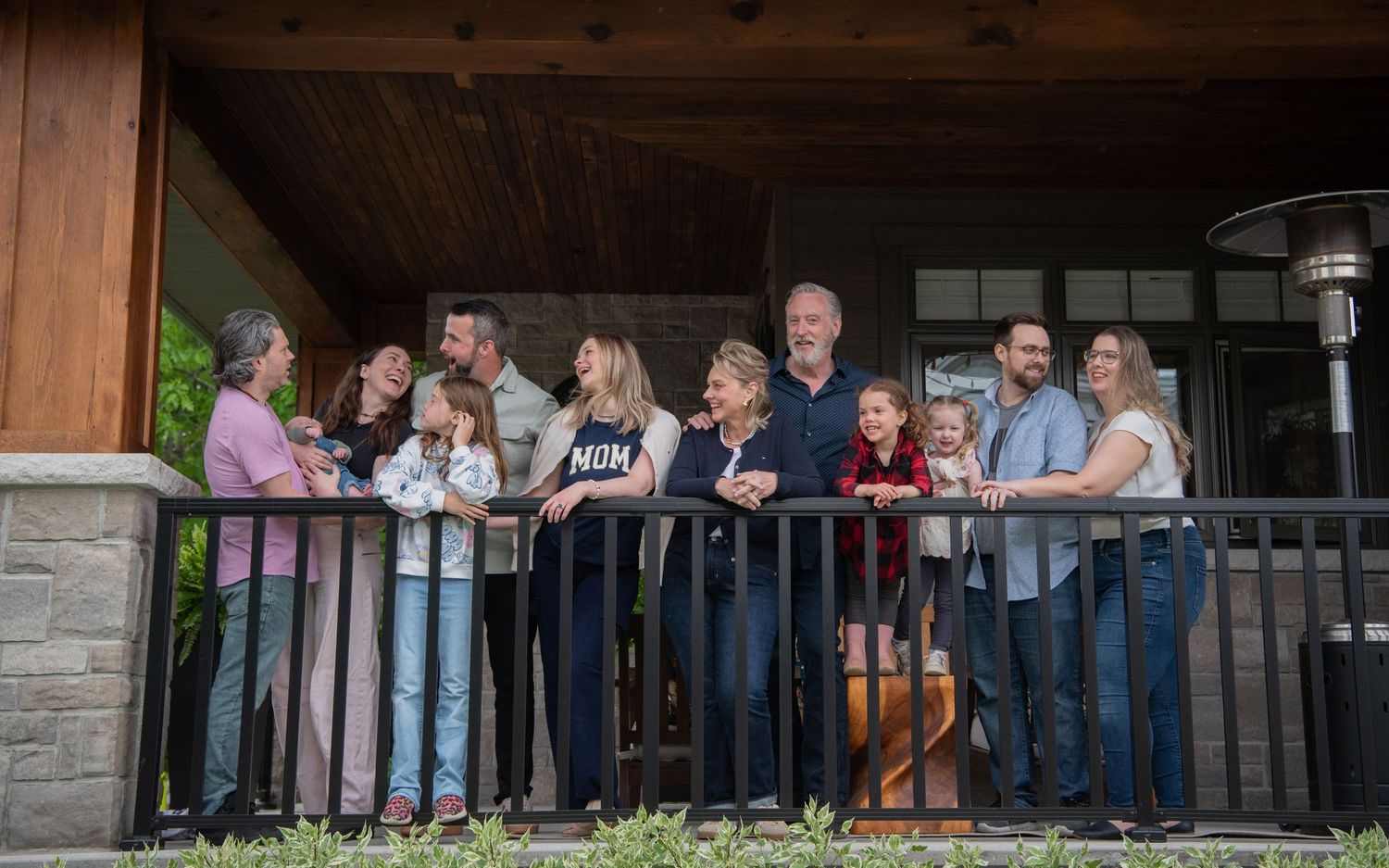 A group of people gathered together on a rustic wooden porch railing at a cabin or lodge.