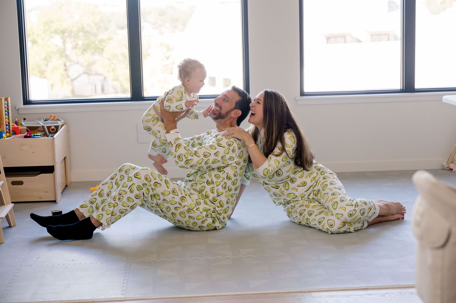 Two people in floral print outfits share a tender moment on the floor near a window.