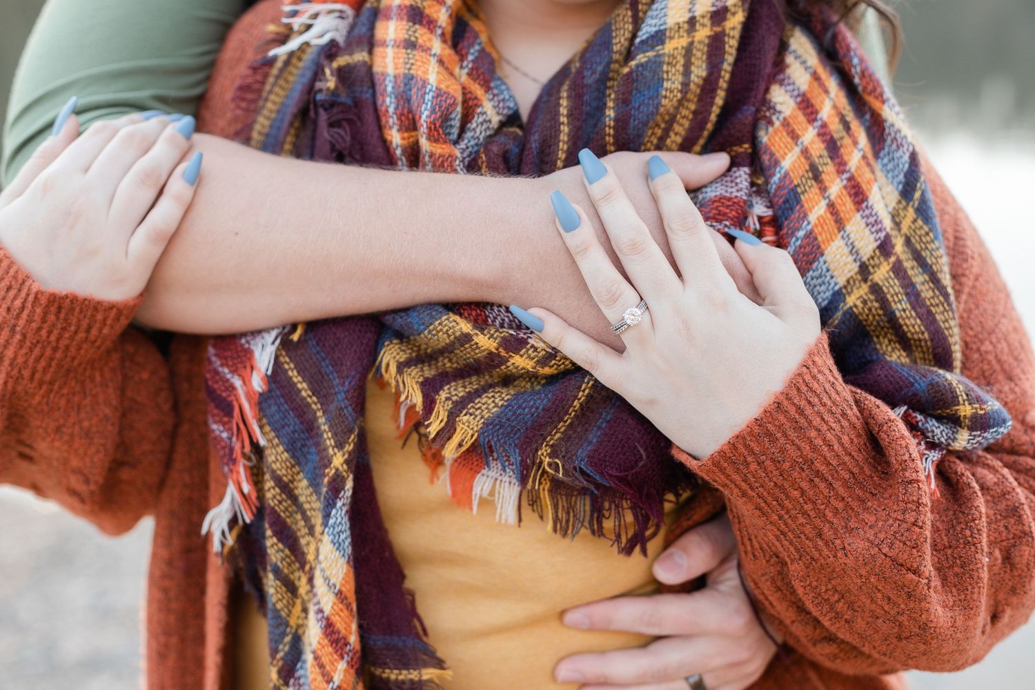 Close-up of hands wearing cozy autumn sweaters during an engagement photoshoot.