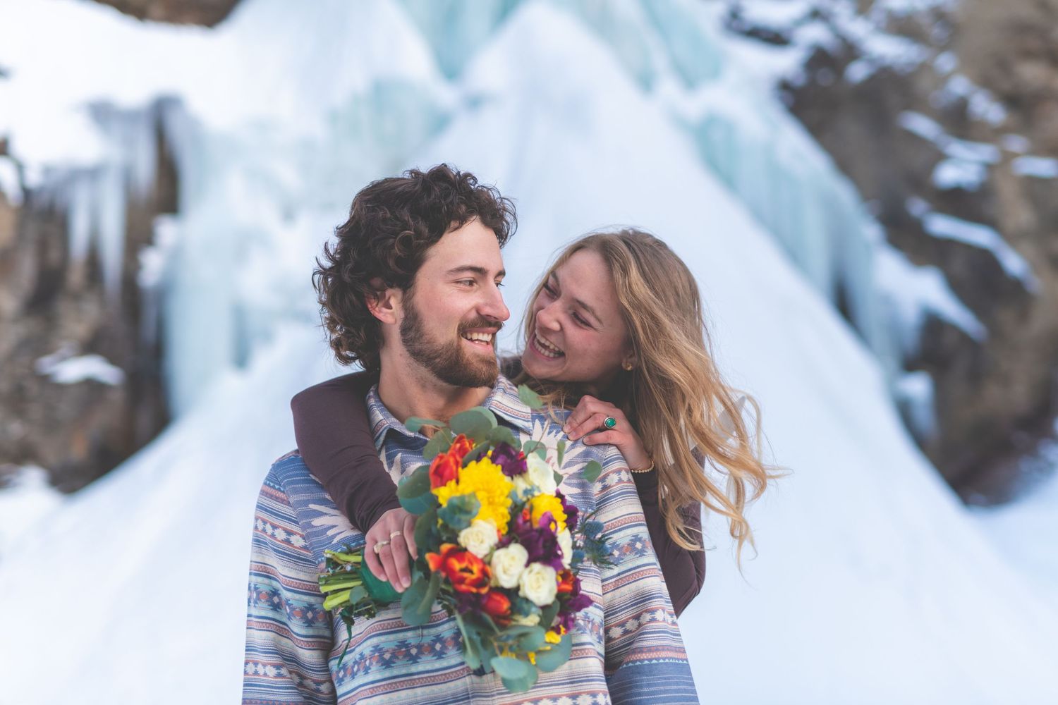 laughing couple with wedding bouquet in front of frozen waterfall in colorado