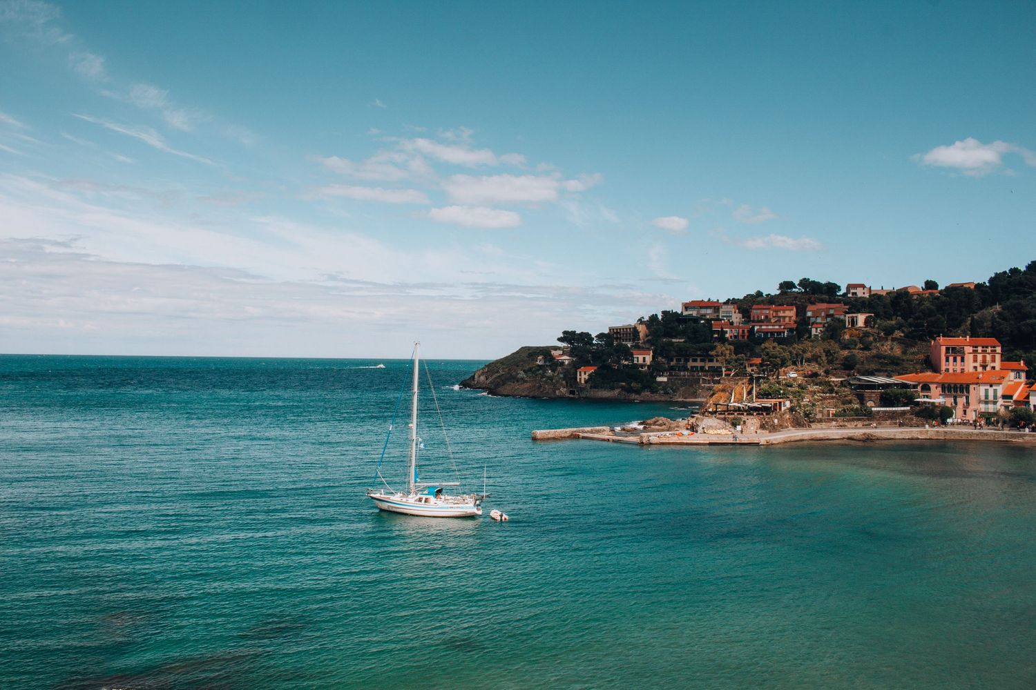 Sailboat anchored in turquoise bay near coastal Mediterranean town.