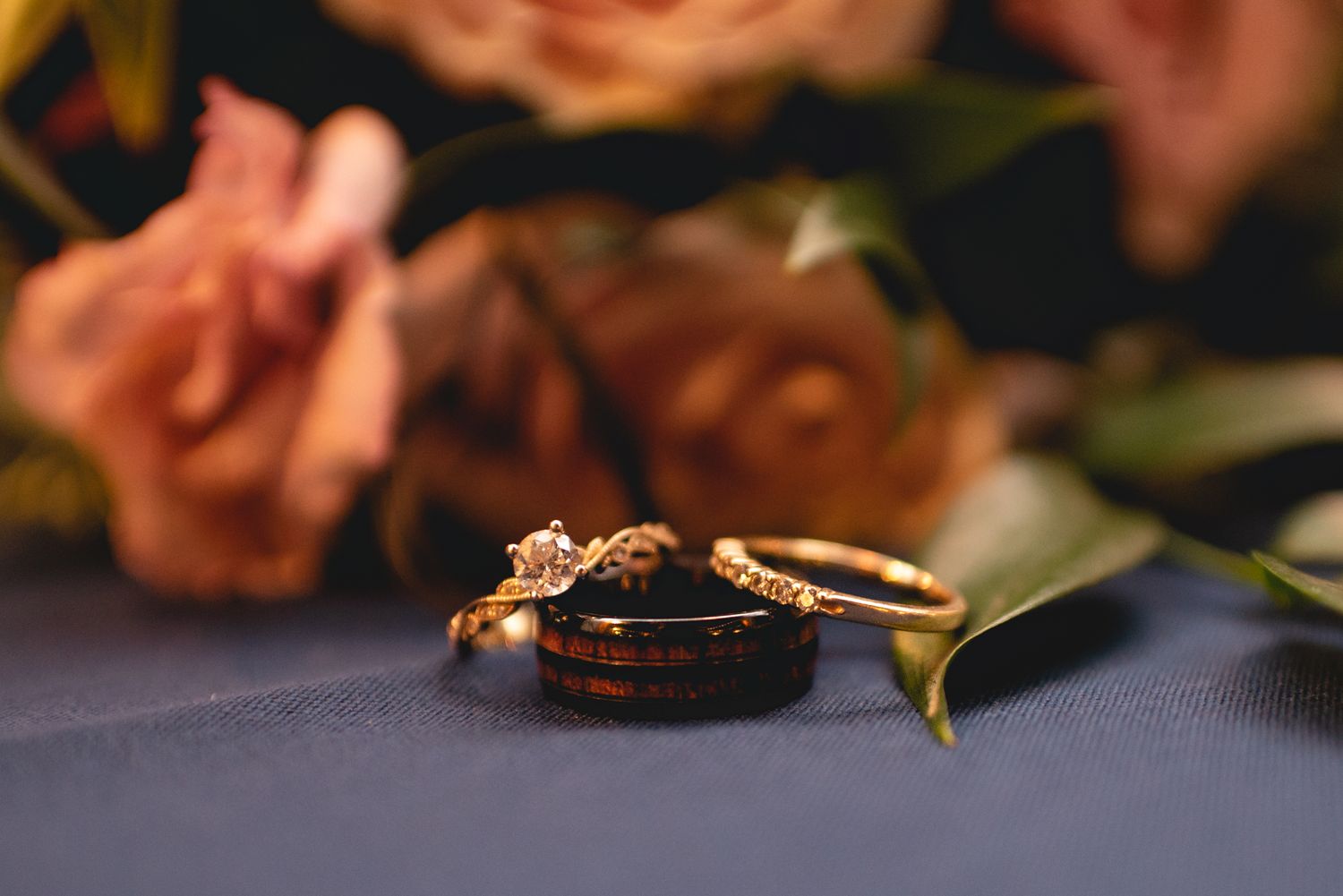 Wedding rings artistically arranged with soft pink roses on a navy blue surface.