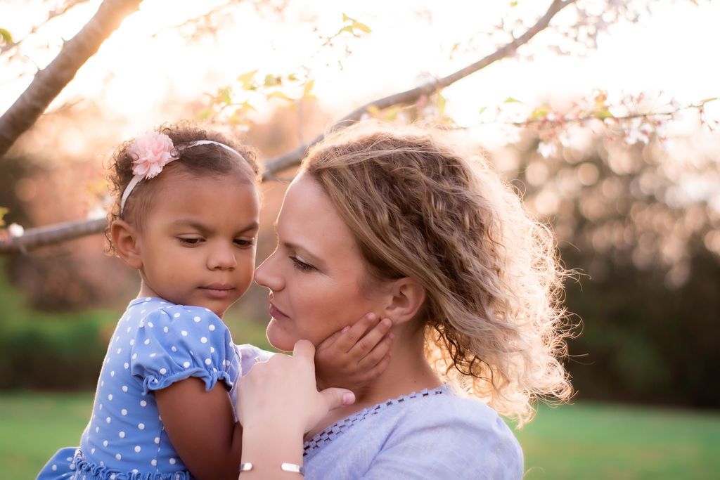 Mother and daughter share a moment in front of a budding cherry tree in spring. Both are wearing blue dresses.