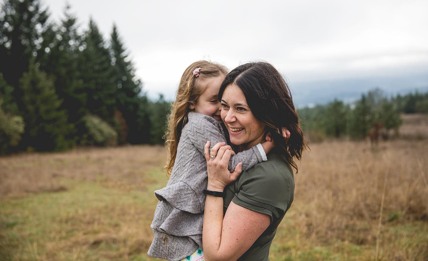 mother holding daughter while daughter whispers in her ear