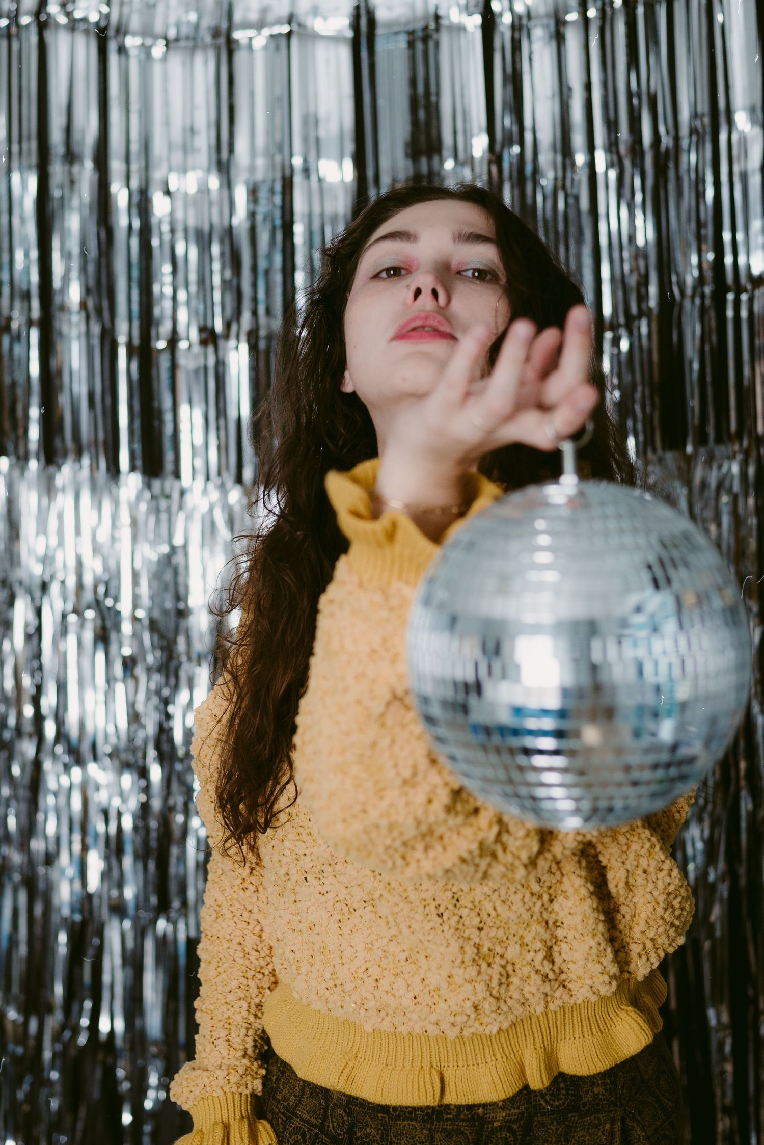 Person in yellow sweater holding disco ball against silver tinsel backdrop.