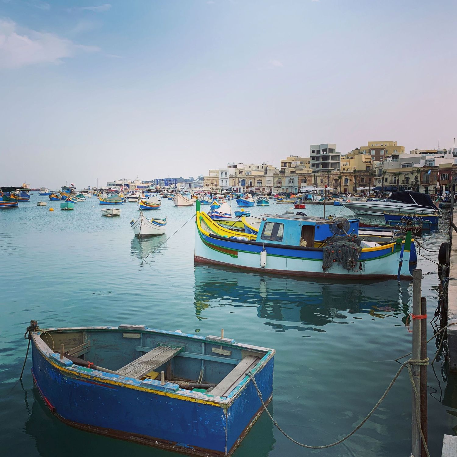 Colorful traditional Maltese fishing boats moored in a calm harbor with town backdrop.