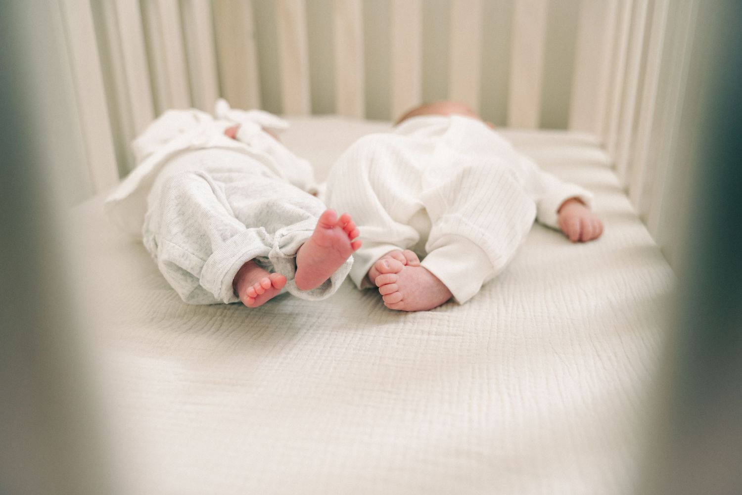 Two tiny pairs of baby feet in white clothing against white crib bedding.