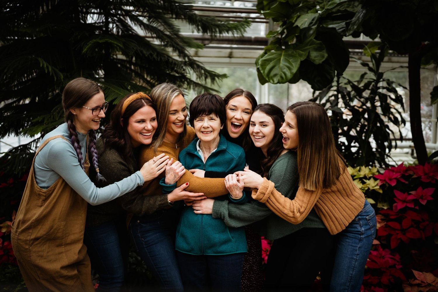 Group of people toasting with drinks in a greenhouse with tropical plants and poinsettias.