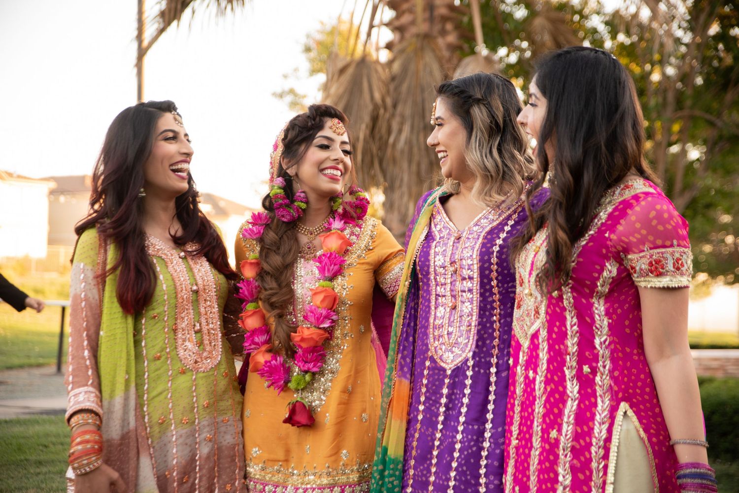 Friends in colorful traditional attire sharing laughs during outdoor wedding festivities.