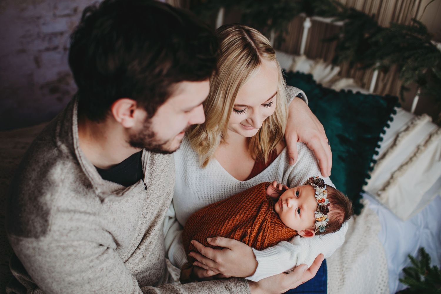 Intimate family photoshoot with newborn in rust-colored wrap against neutral backdrop.