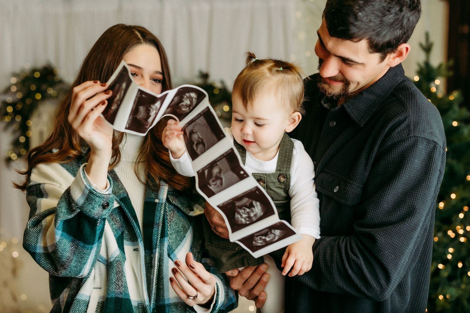 Family looking at ultrasound photos together near Christmas decorations with joyful expressions.
