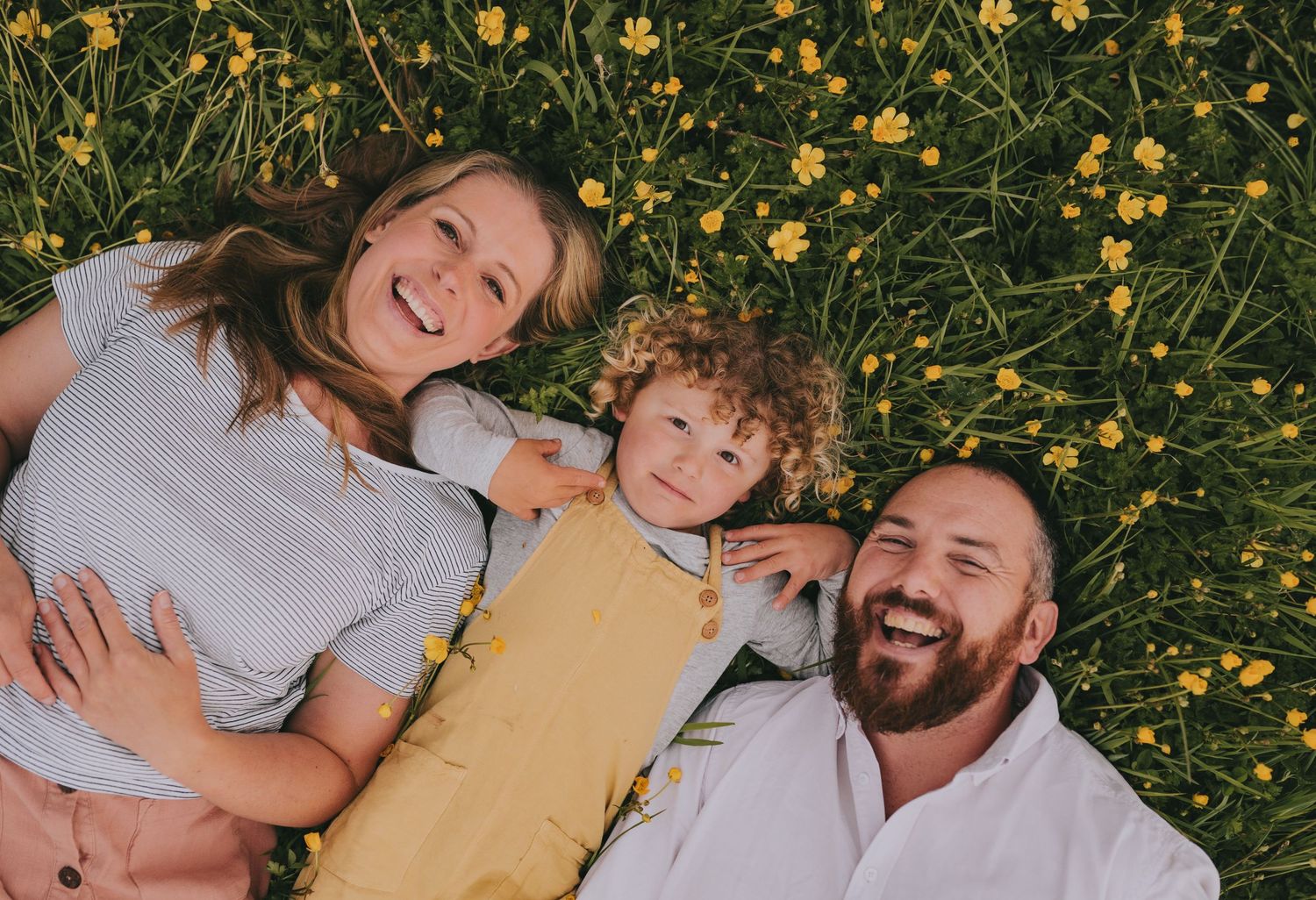 Family lying in a field of yellow wildflowers sharing happy smiles.