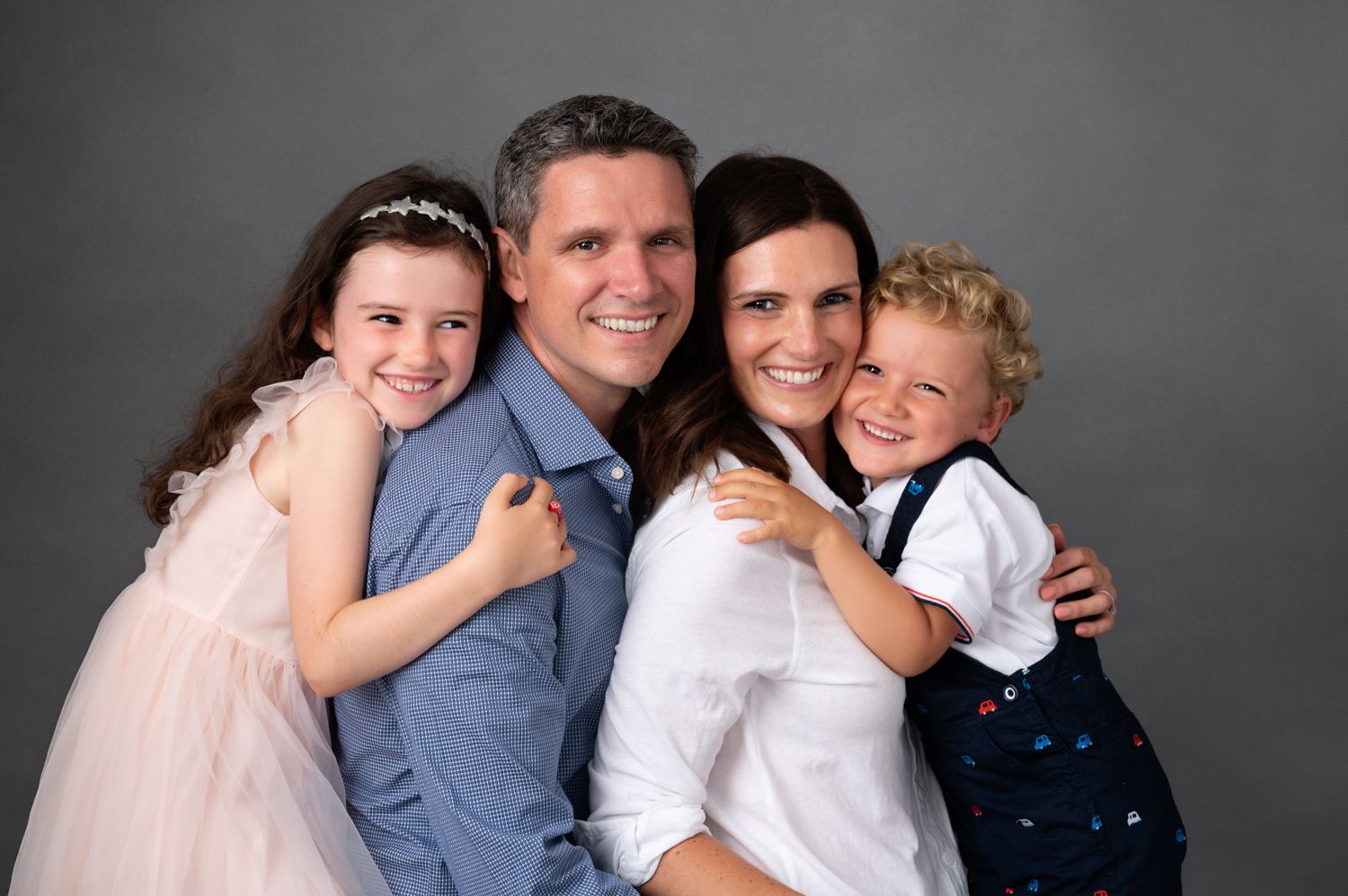 Portrait of a family against a gray backdrop in coordinated casual attire.